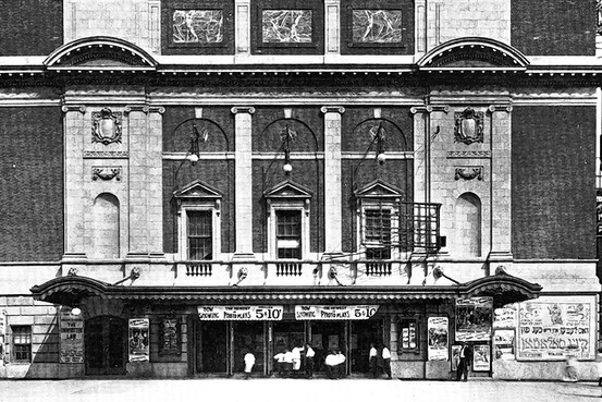 Historic theater building facade with decorative columns and arches, featuring posters and a marquee advertising a 5 and 10 cent pricing.