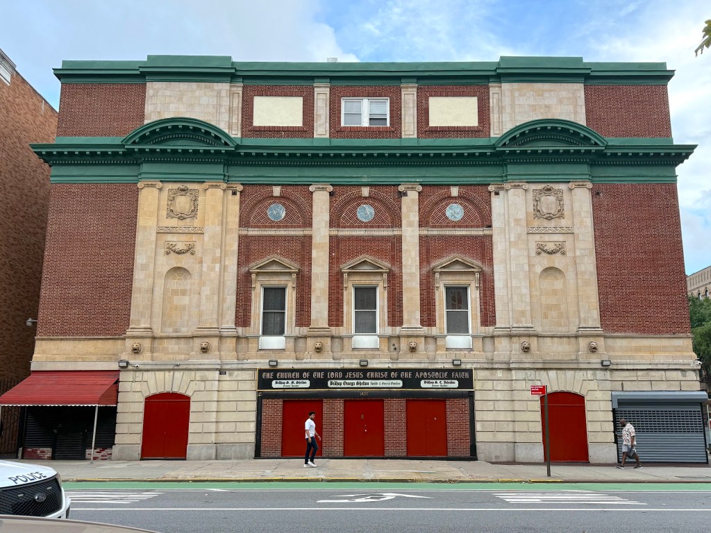Facade of a brick building with decorative elements, featuring the sign 'The Church of the Lord Jesus Christ of the Apostolic Faith' and red doors.