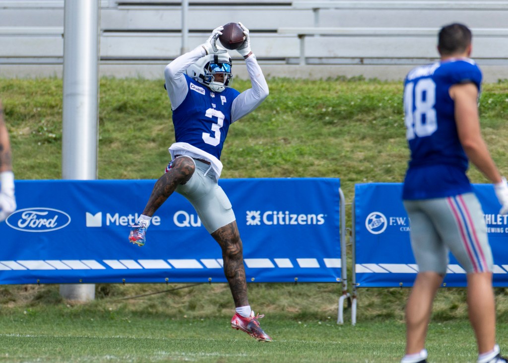 Odell Beckham, Jr. wearing a blue New York Giants jersey and white helmet, catches a football during training camp.