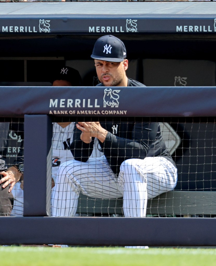 Giancarlo Stanton in a New York Yankees cap reacting on the dugout fence.
