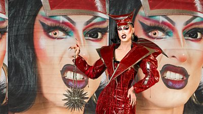 Drag Queen Coral wearing a red leather dress and holding a metal spike ball on a chain