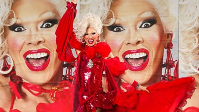 Drag Queen Danni wearing a bright red sparkly dress with various frills and fabric coming from it