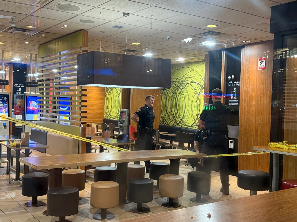 Two police officers stand in a McDonald's restaurant cordoned off with yellow crime scene tape.