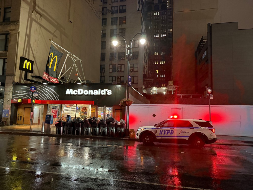 An NYPD police car with flashing red lights is parked outside a McDonald's restaurant at night.