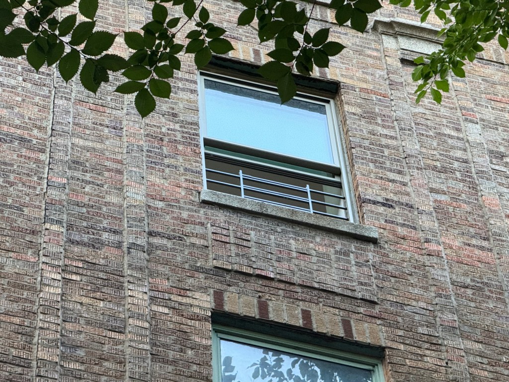 A brick building with windows, one of which has a metal guardrail.