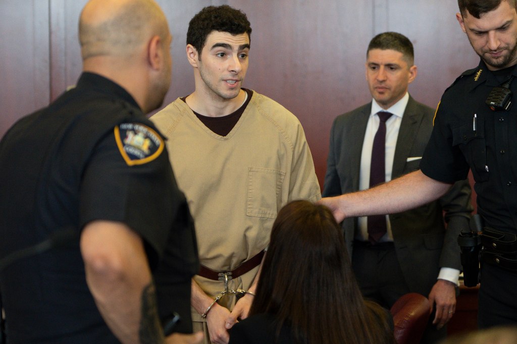 Luigi Mangione, accused of killing UnitedHealthcare CEO Brian Thompson, appears in court wearing a tan jumpsuit and handcuffs, surrounded by officers.