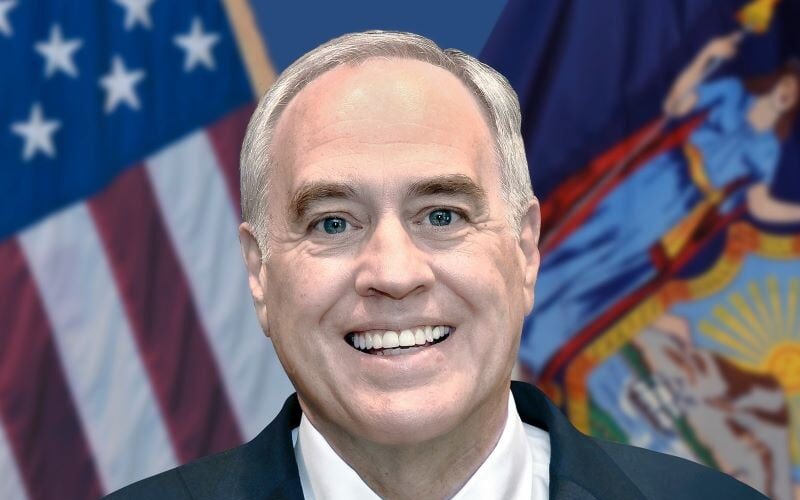 New York State Comptroller Thomas DiNapoli smiles in front of American and New York flags.