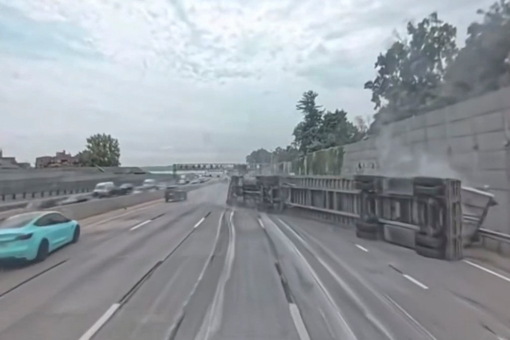A tractor-trailer lying on its side on a multi-lane highway after colliding with an overpass.