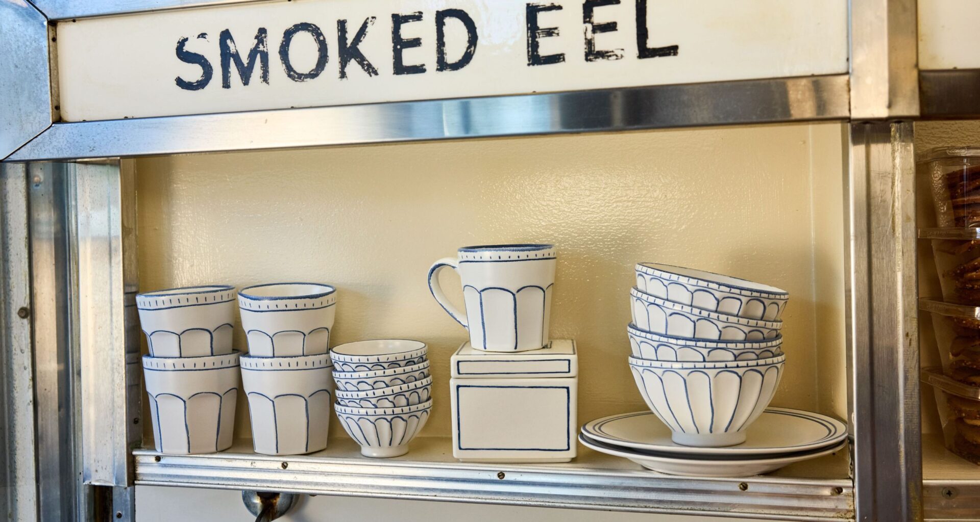 Russ &amp; Daughters x West Elm white ceramic serveware lined in blue pictured atop a mid-century style shelf framed in chrome