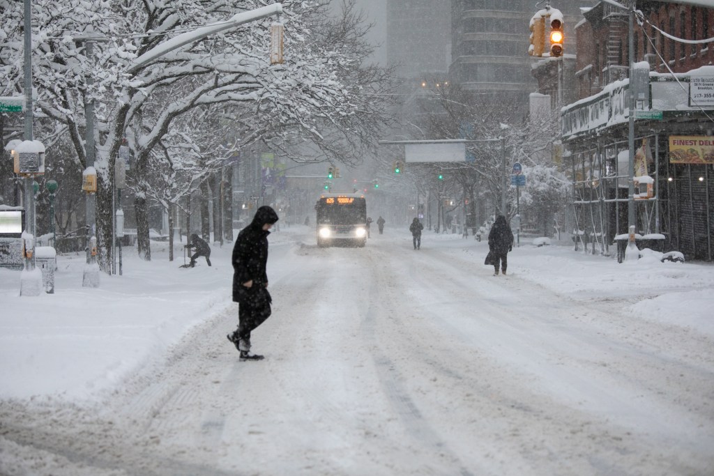 People trudge through the snow while buses run along empty Brooklyn streets during a blizzard,