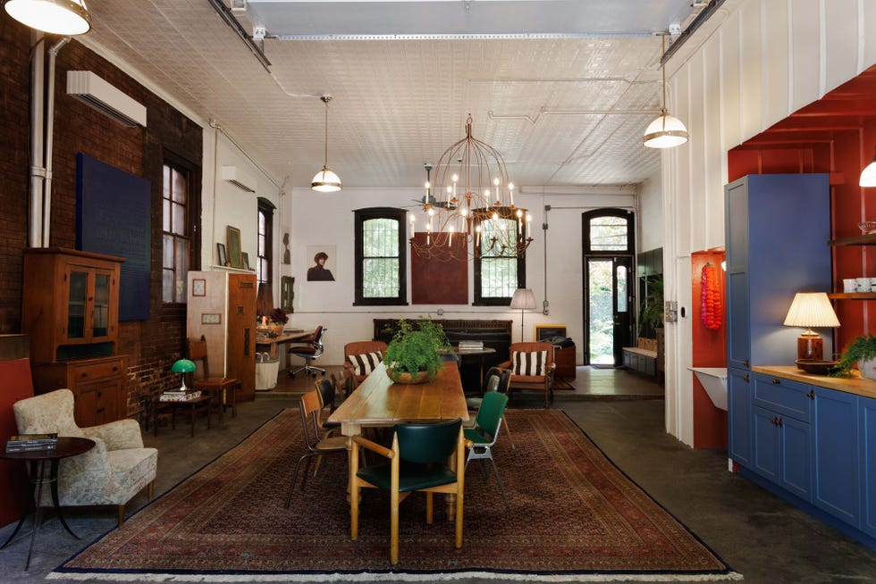 Stylish dining area with eclectic furniture, chandelier, and large windows, featuring a rich patterned rug and plant decor.