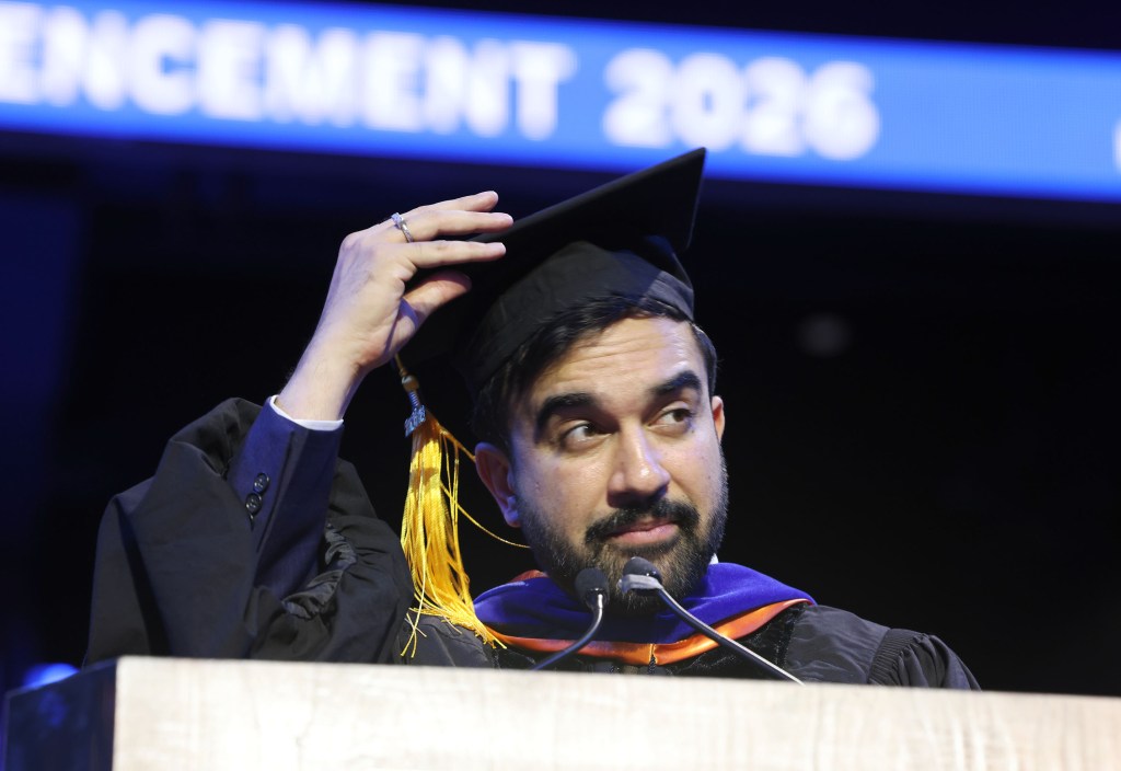 Zohran Mamdani, wearing a graduation cap and gown, at a podium with microphones.