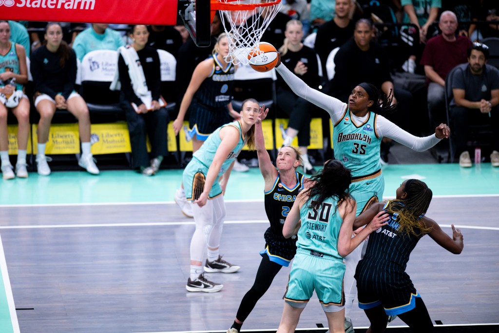 Jonquel Jones blocks a shot at the rim while Sabrina Ionescu looks on in front of the Liberty's bench. 