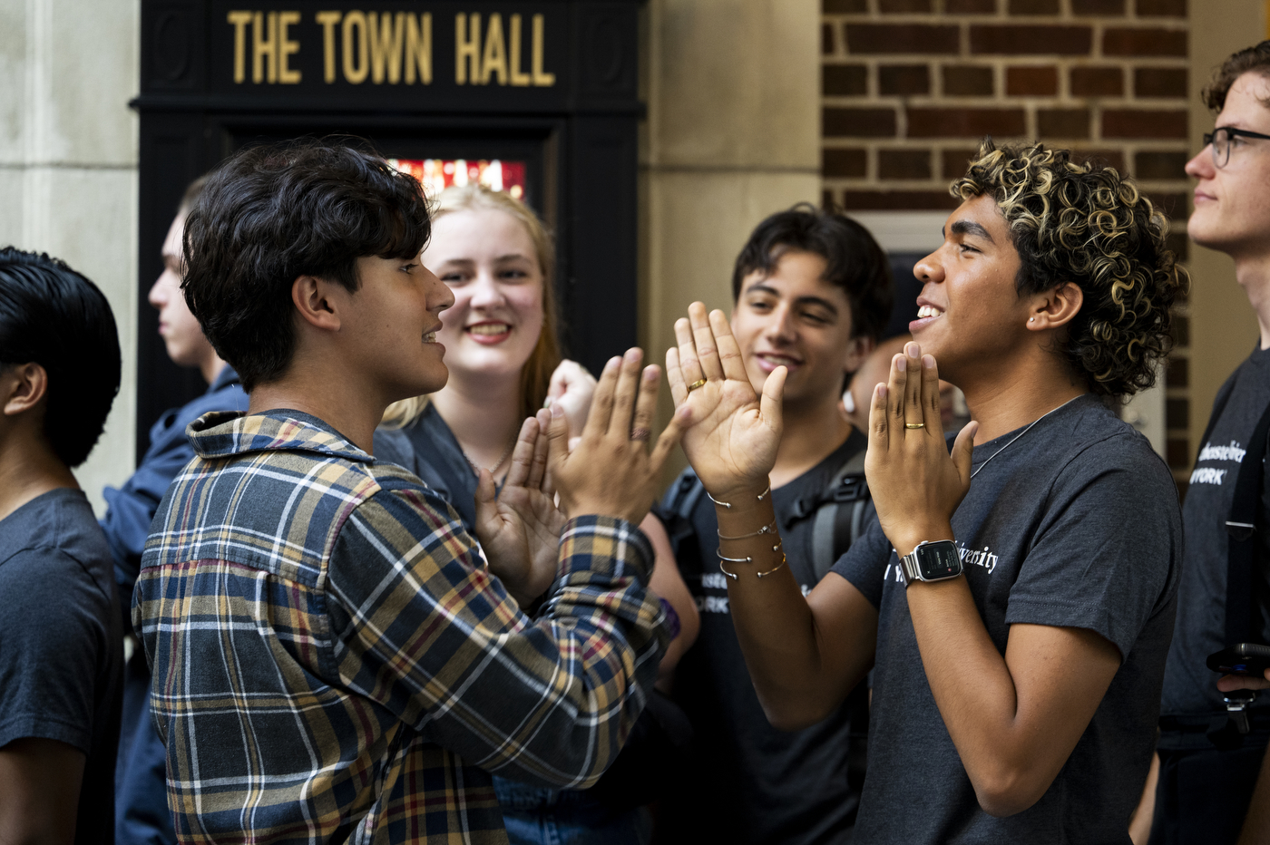 Students in Northeastern University T-shirts gather outside The Town Hall in New York City, smiling and giving high fives during the university’s city convocation.