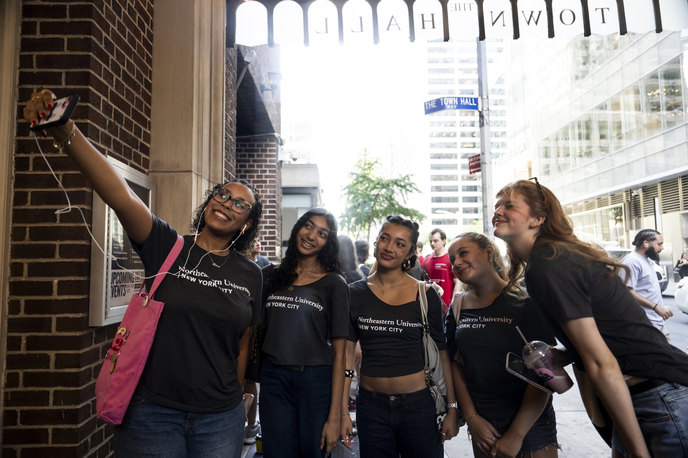 Students in Northeastern University T-shirts gather outside The Town Hall in New York City, smiling and giving high fives during the university’s city convocation.