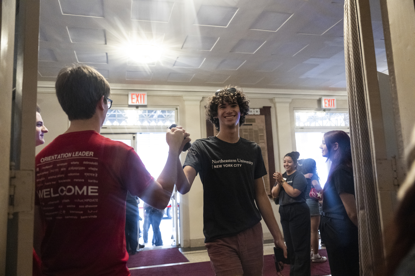 Students in Northeastern University T-shirts gather outside The Town Hall in New York City, smiling and giving high fives during the university’s city convocation.