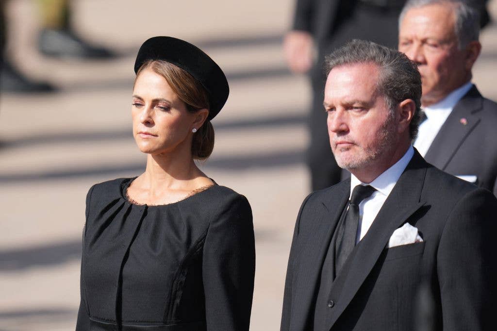 Princess Madeleine, Duchess of Hälsingland and Gästrikland, in black dress and hat, stands with a man in a black suit.