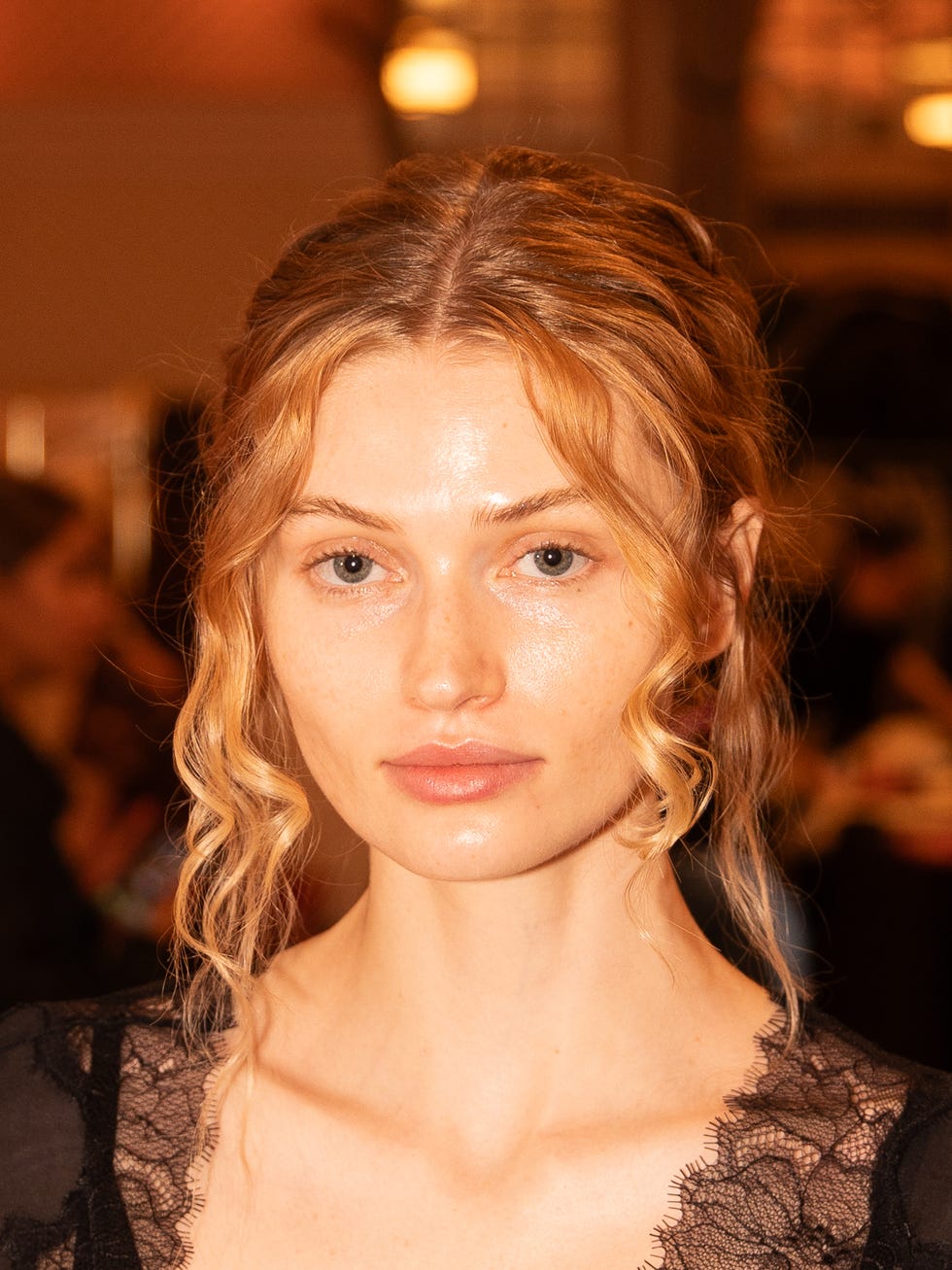 Model with wavy hair and natural makeup, wearing a black lace top, posing against a softly lit background. Model with wavy hair and natural makeup, wearing a black lace top, posing against a softly lit background.