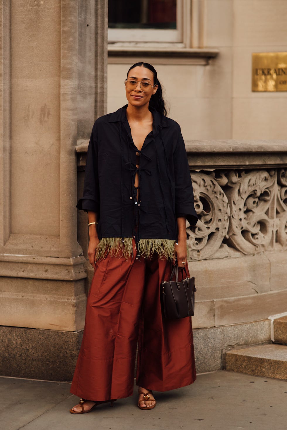 Woman in a stylish outfit with a knotted top and wide-leg pants, standing against a decorative building. Woman in a stylish outfit with a knotted top and wide-leg pants, standing against a decorative building.