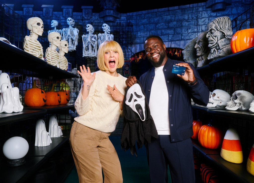 A woman and a man pose in a Halloween-themed store aisle filled with spooky decorations, with the man holding a "Scream" mask and a Chase Freedom Flex card.