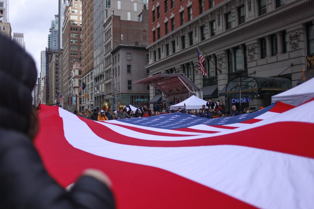 Veterans Day parade goers hold a gian American flag while moving up Fifth Avenue in Manhattan,