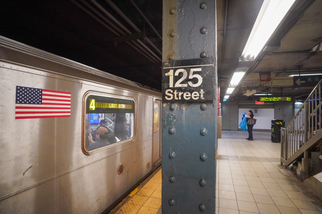 Subway station with a train displaying an American flag sticker and the 125th Street sign.