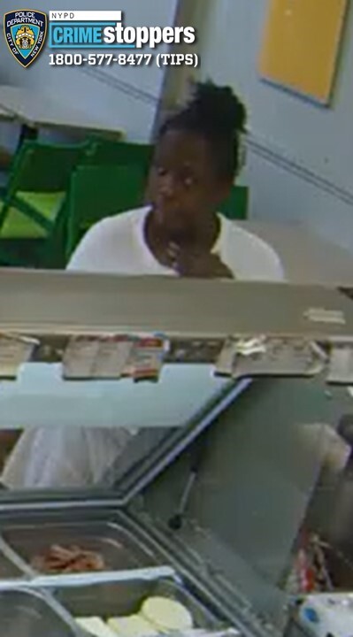 A person with dark hair in a bun and a white shirt looks to the right, behind a counter with ingredients.