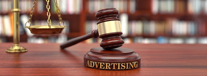 A judges gavel labeled Advertising rests on a wooden desk, with a scale of justice and blurred bookshelves in the background, symbolizing legal issues related to advertising.