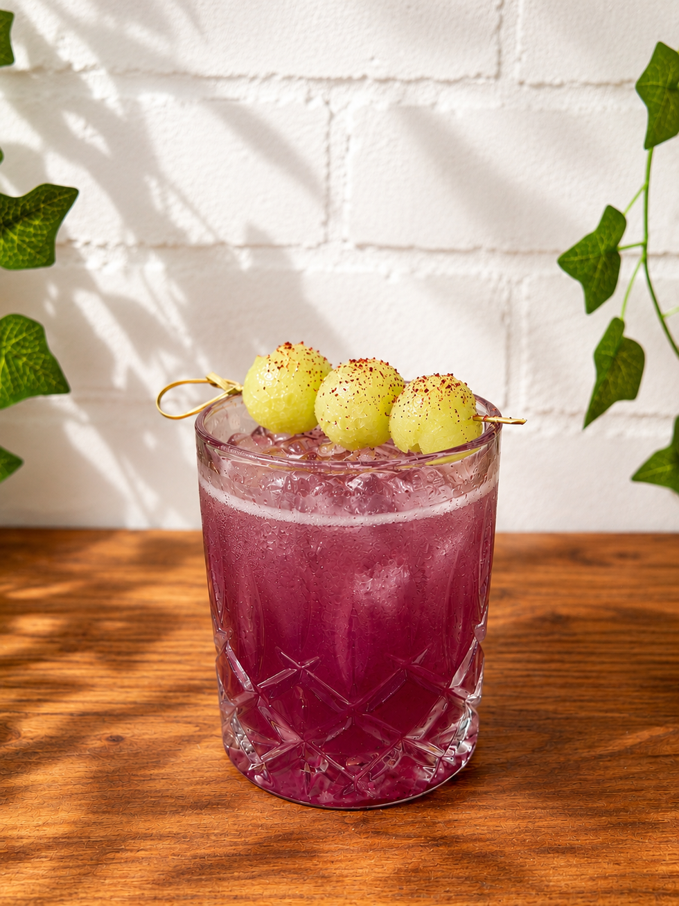 A refreshing purple drink garnished with green melon balls, served in a crystal glass on a wooden table.