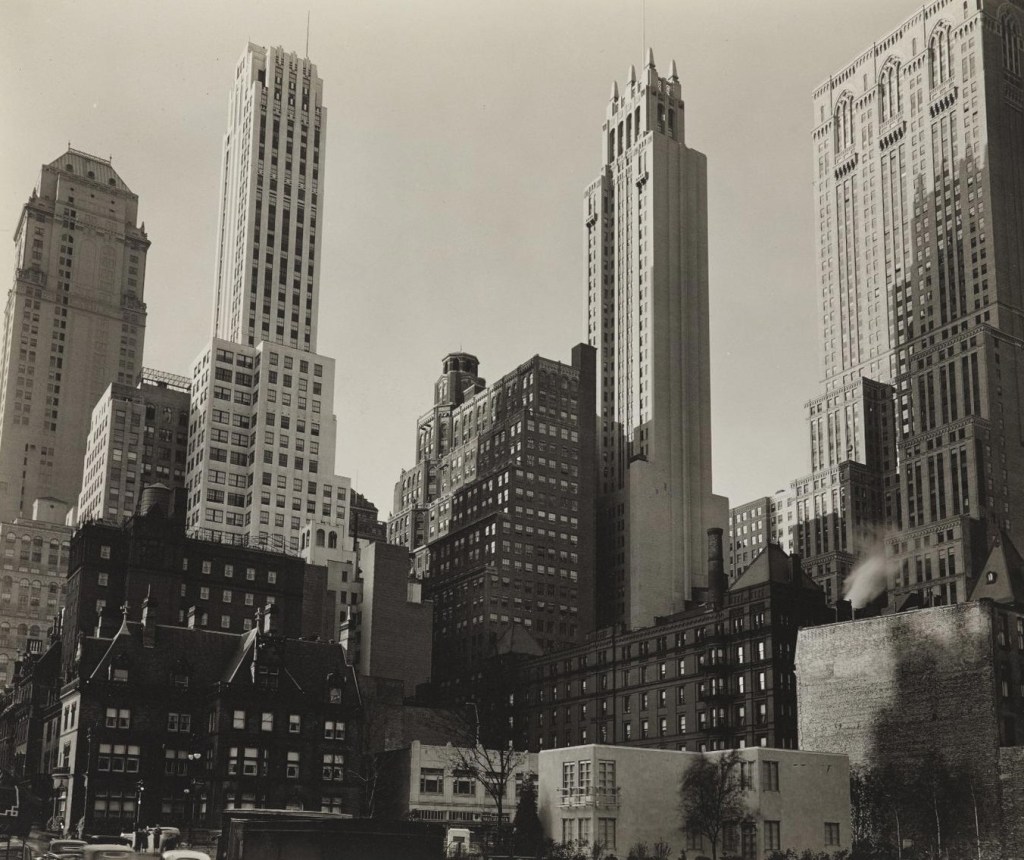 Black and white photo of a city skyline featuring a mix of modern and older architectural buildings, with several skyscrapers towering over a distinct lower building area.