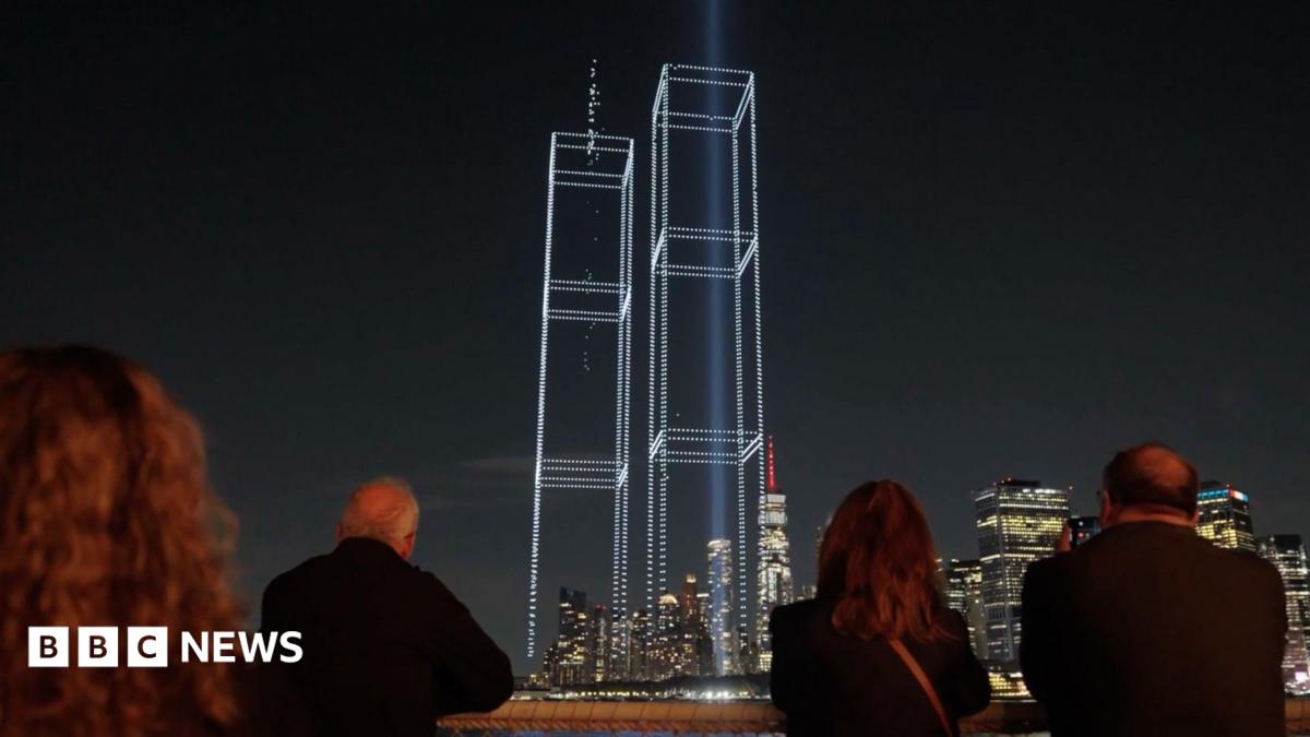 A group of people watching a drone light display showing the Twin Towers.