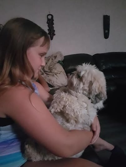 A young girl hold a small dog in her lap and looks at him adoringly.