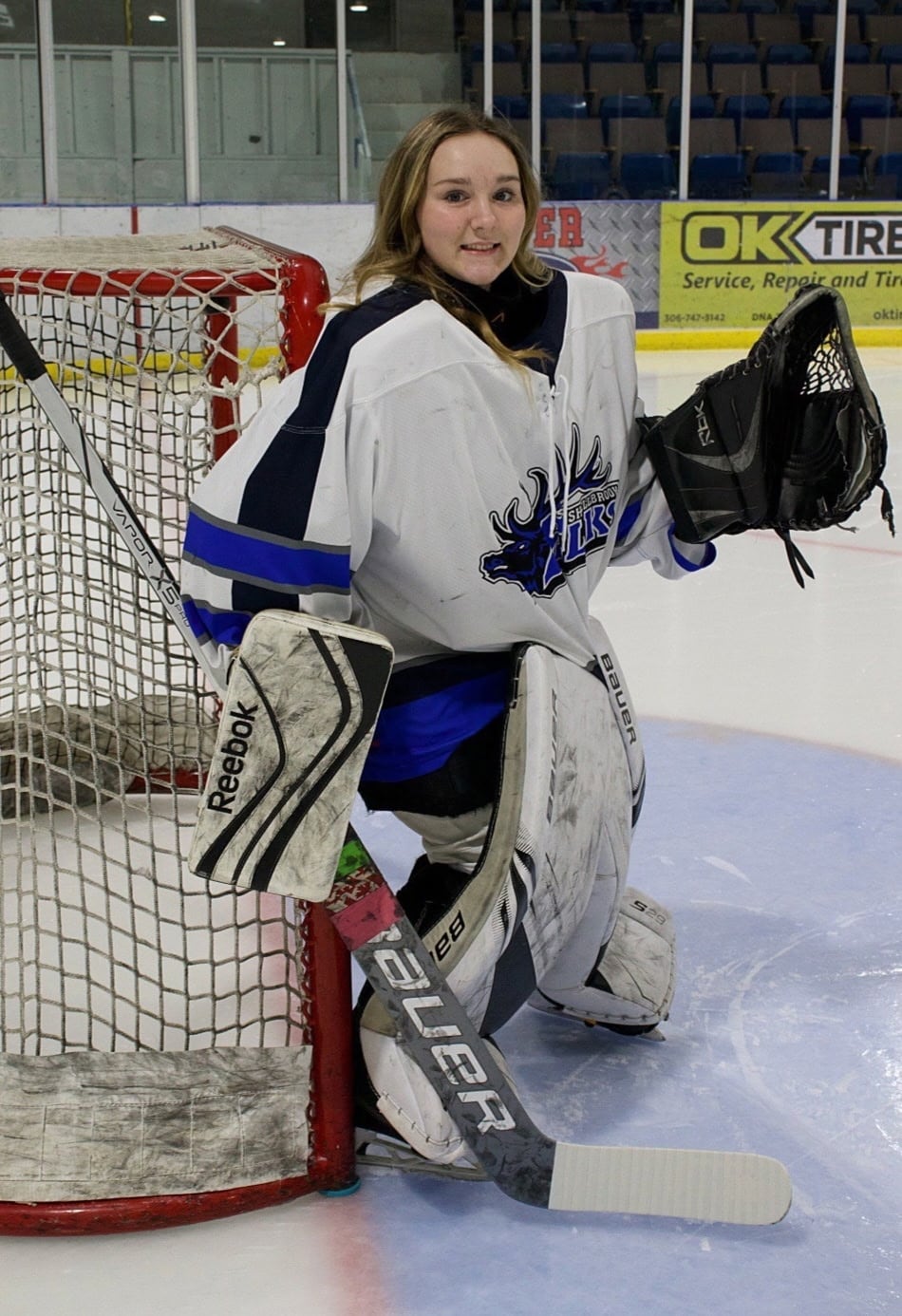 A girl in a goalie uniform poses in a hockey net.