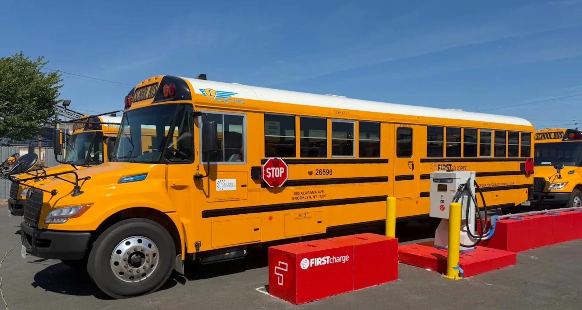 An electric school bus parked near a charging station with another bus in the background.