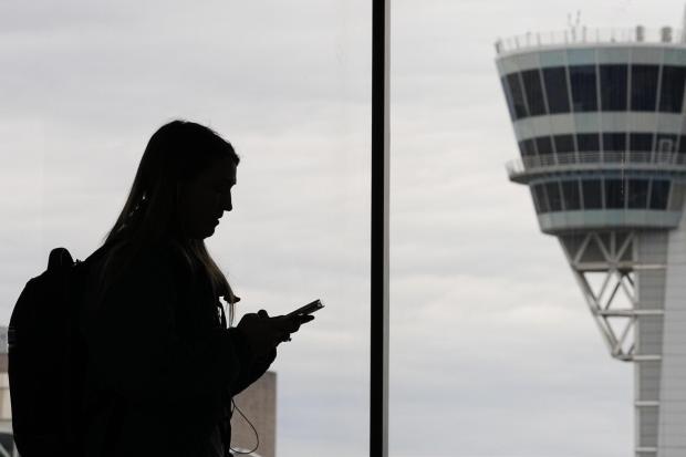 A traveler with a smartphone walks past an air traffic control tower at Philadelphia International Airport.