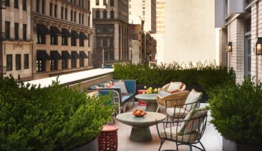Rooftop terrace of a New York hotel with lush greenery, comfortable seating, and city buildings in the background.