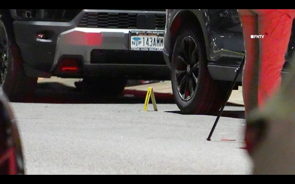 A yellow evidence marker on the street near parked vehicles at a crime scene.