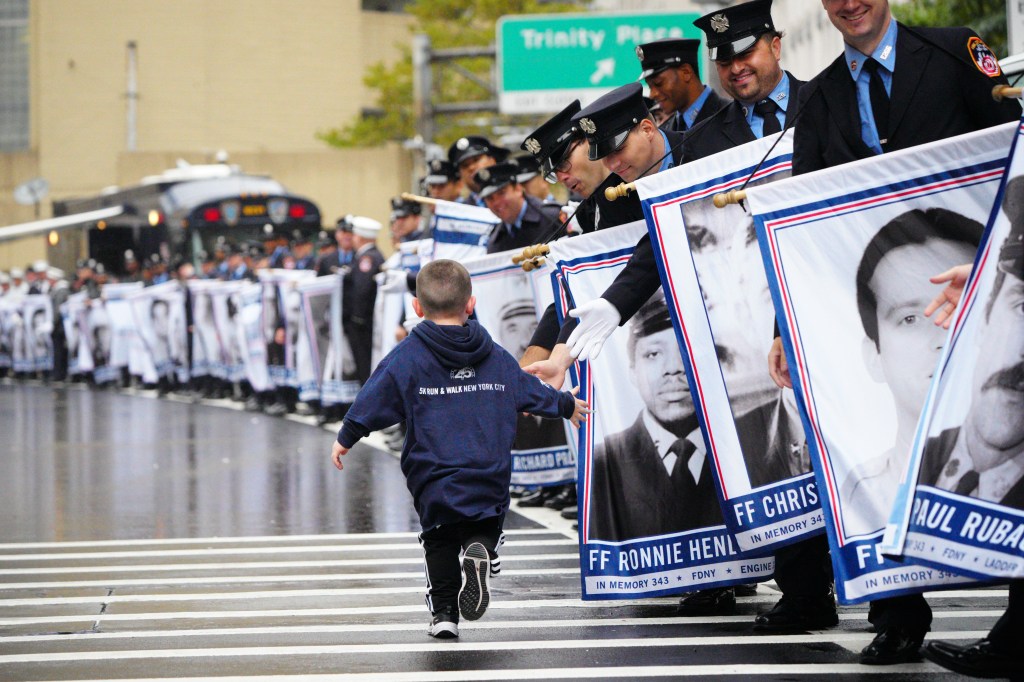 A runner in a blue hoodie and sweatpants runs along a row of firefighters holding banners with images of fallen firefighters.