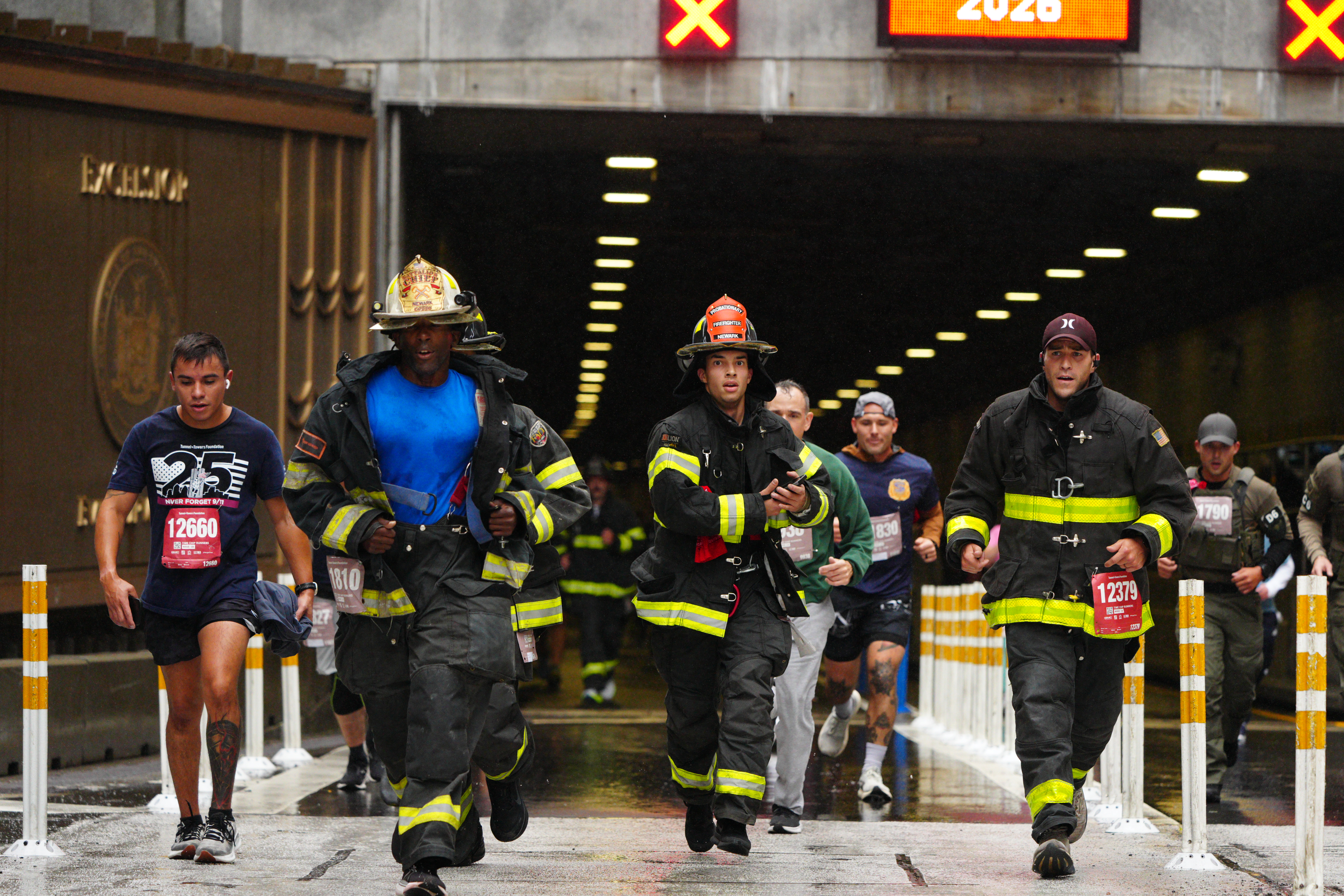 Participants, including firefighters in full gear and a runner with a race bib, run in the 25th annual Tunnel to Towers NYC 5K Run & Walk.