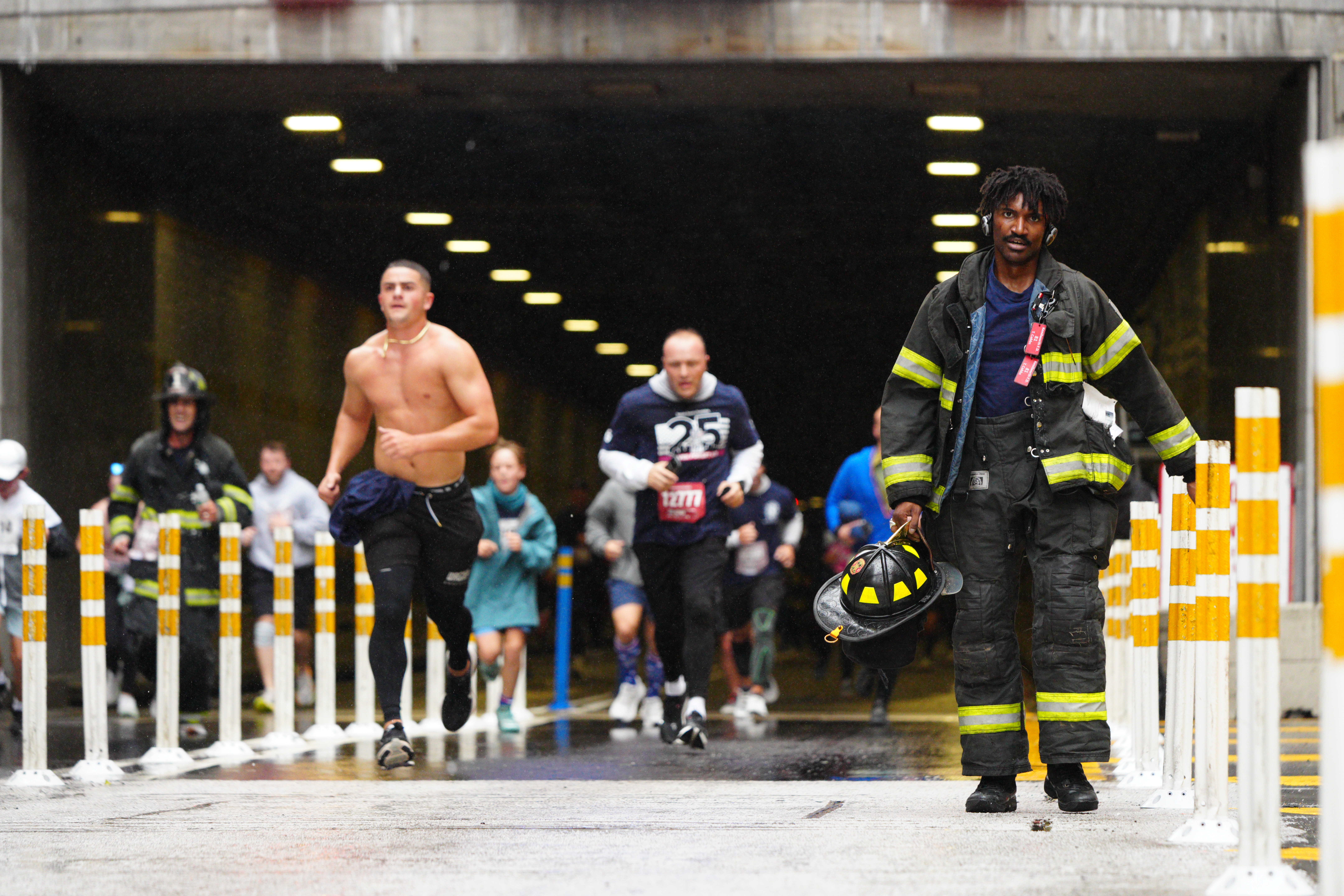 A man dressed in firefighter gear holds his helmet as participants run in the Tunnel to Towers NYC 5K Run & Walk.
