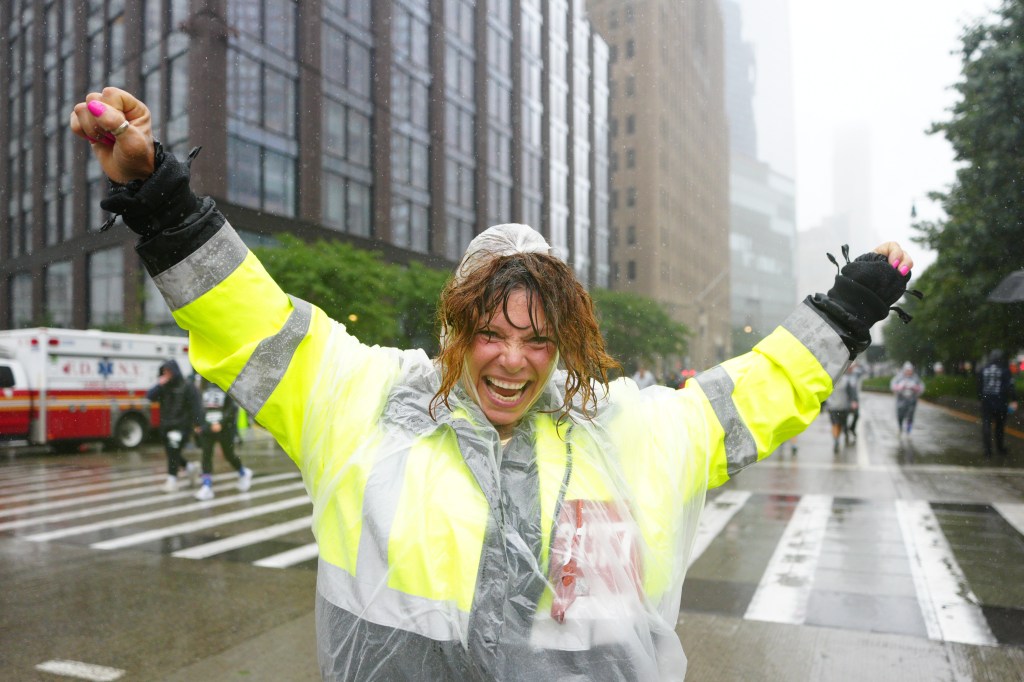 A woman in a neon yellow safety vest and clear poncho cheers with her arms raised during the Tunnel to Towers 5K Run & Walk.