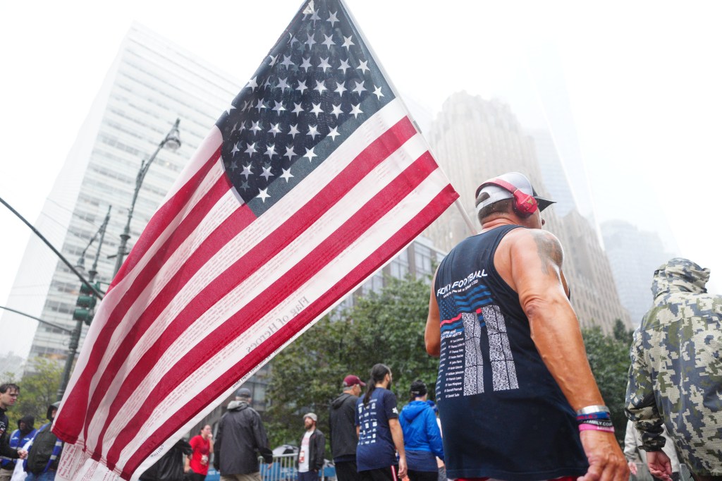 People participate in the Tunnel to Towers NYC 5K Run & Walk, with an American flag prominent in the foreground.