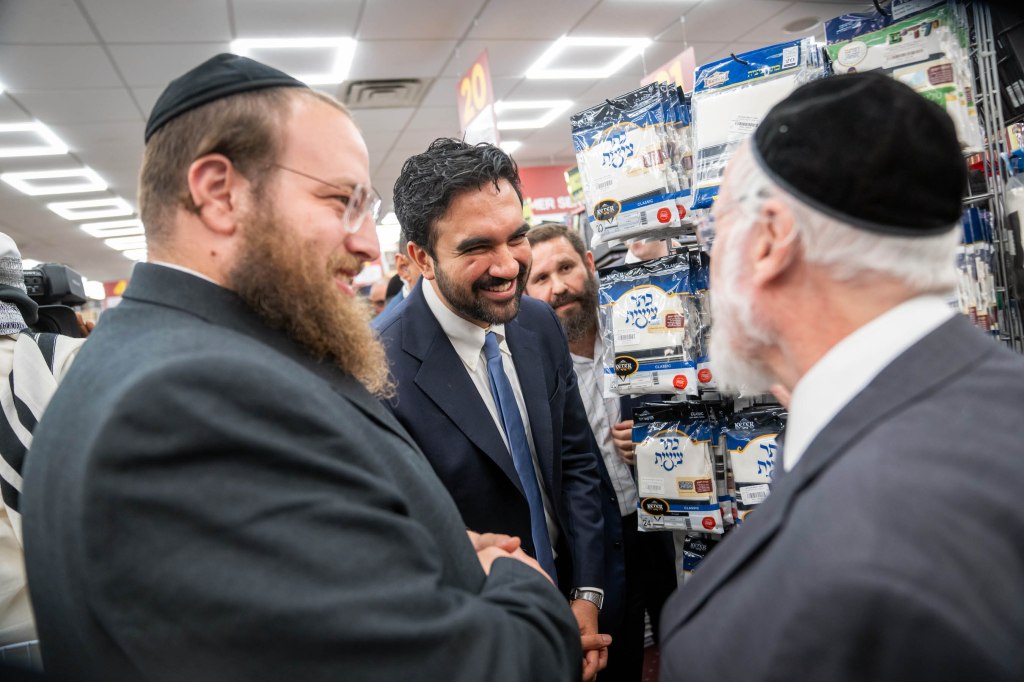 Mayor Zohran Mamdani smiling while visiting Eichler's Judaica store and interacting with two men.