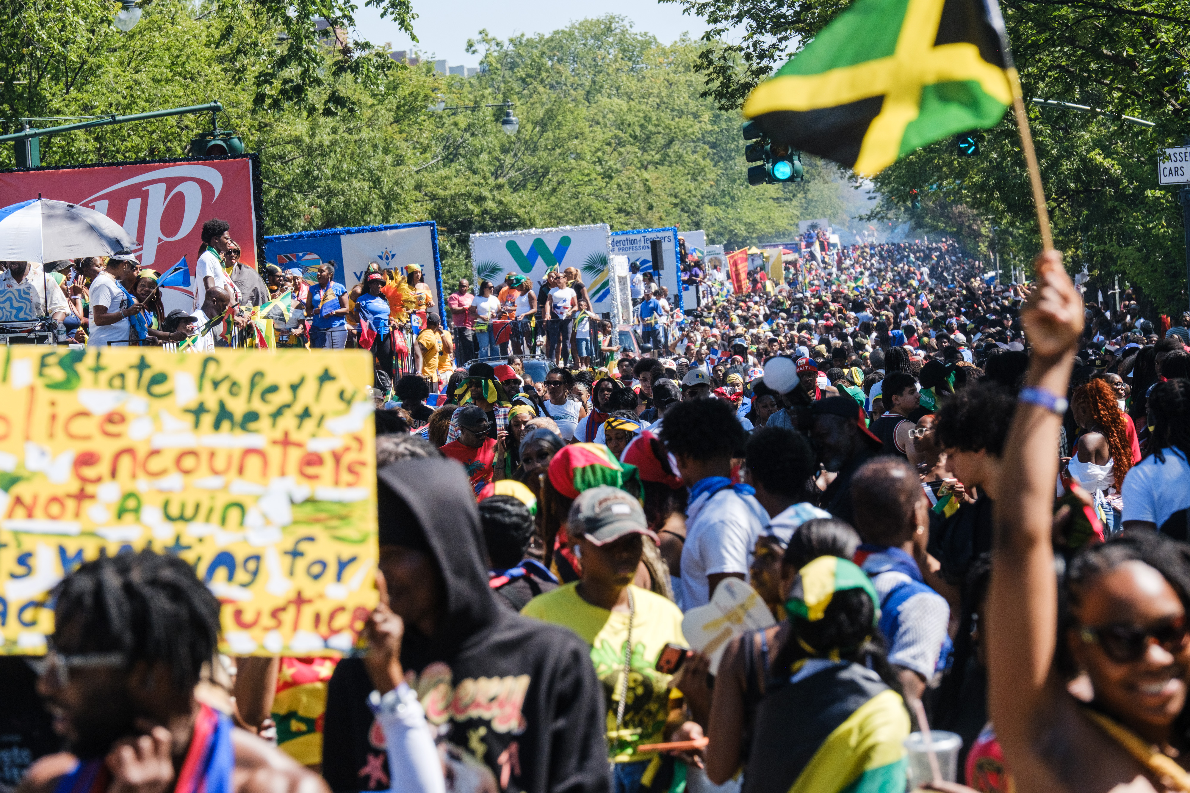 Crowds of people gather for the West Indian Day Parade in Crown Heights, Brooklyn, with a Jamaican flag prominent in the foreground.