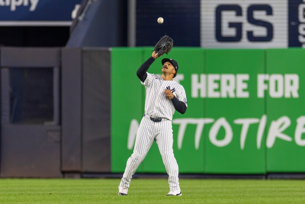 A New York Yankees player looking up to catch a baseball.