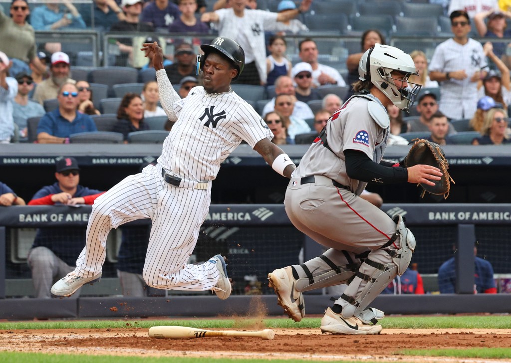 A New York Yankees batter jumps after hitting a baseball, with a Boston Red Sox catcher in a crouched position behind him.