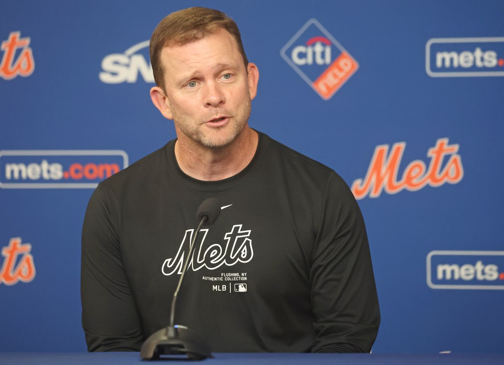 A man in a black long-sleeve shirt with "Mets" written on it speaking into a microphone.