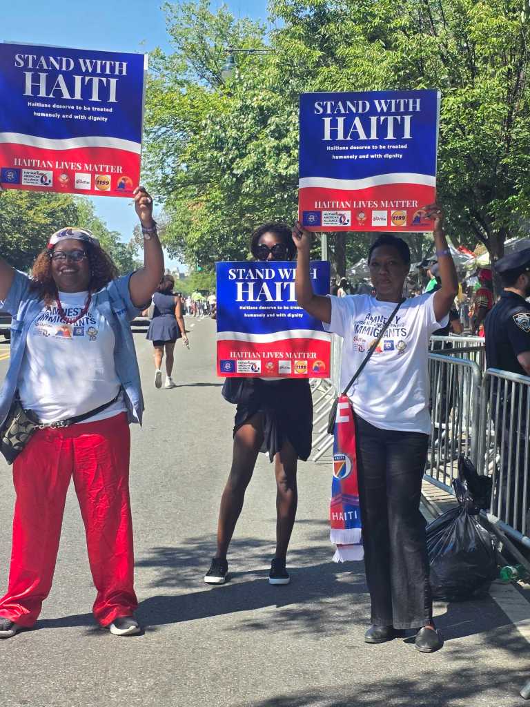 Yolette Williams of the Haitian American Alliance, center, marches with two women carrying a sign calling for the restoration of TPS for Haitians during the West Indian Day Parade in Brooklyn, N.Y., Sept. 7, 2026. Photo by Darlie Gervais for The Haitian Times.
