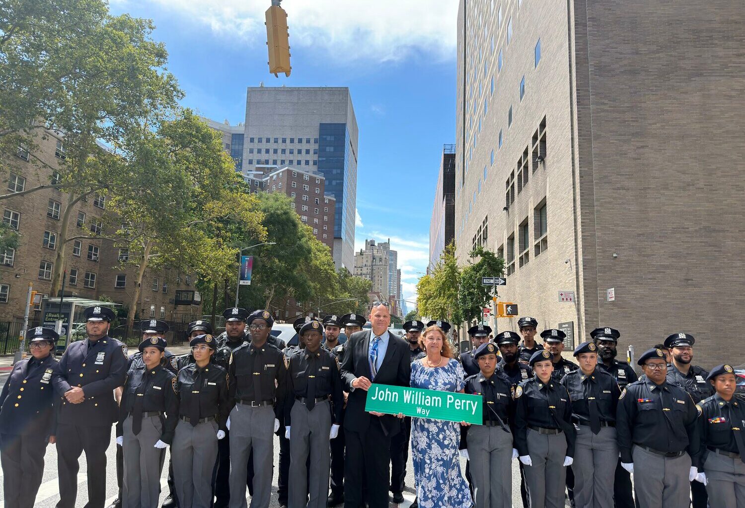 Janice Perry Montoya and Joel Perry hold the new John William Perry Way street sign alongside NYPD officers and members of the NYPD High School Police Explorers.
