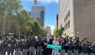 Janice Perry Montoya and Joel Perry hold the new John William Perry Way street sign alongside NYPD officers and members of the NYPD High School Police Explorers.